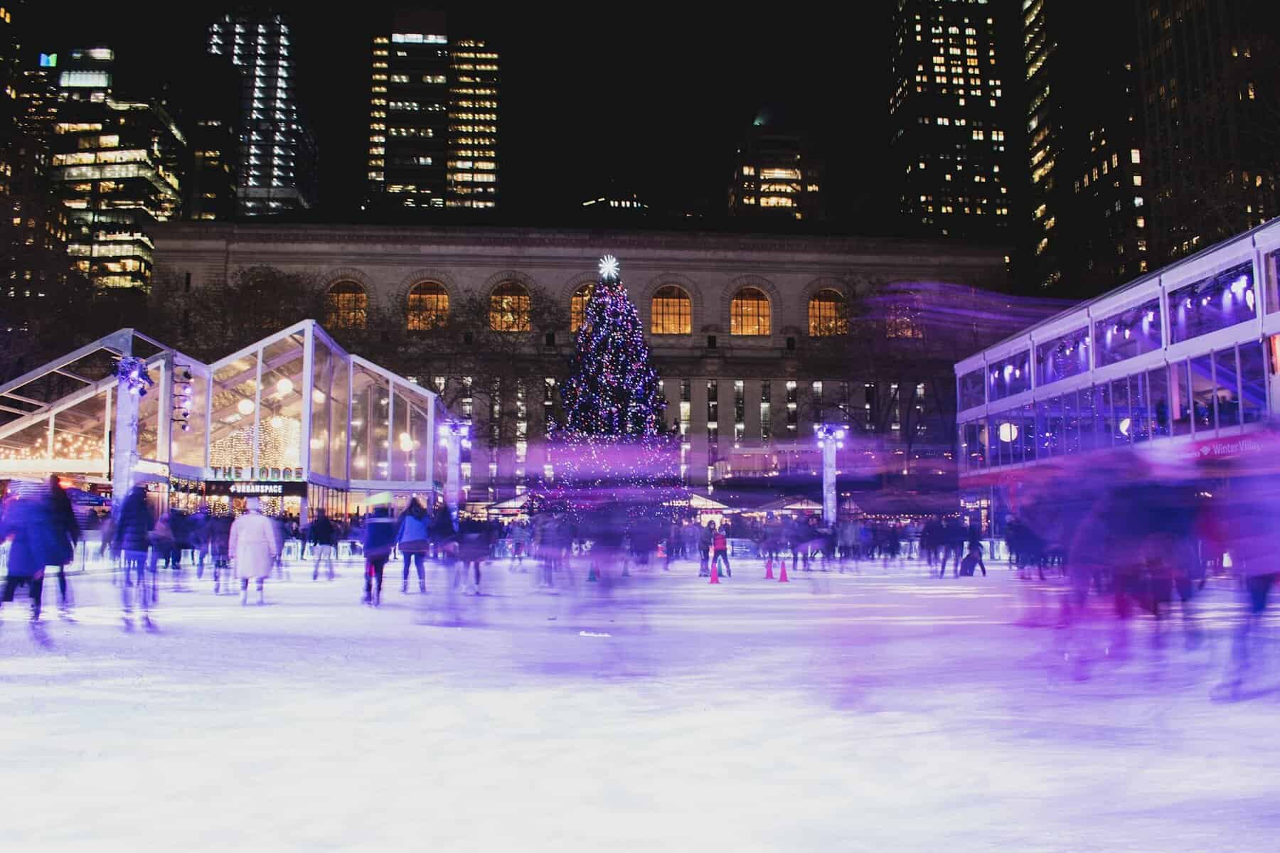 People skating at Rockefeller Center Christmas ice rink with festive city lights and a decorated tree.