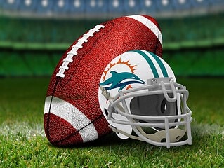 Close-up of American football ball with Miami Dolphins helmet on lush green field.