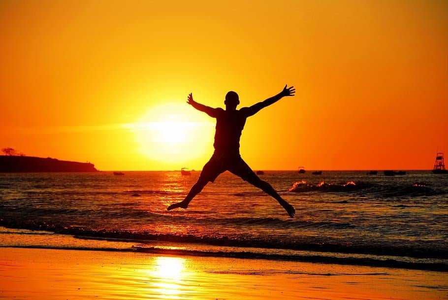 Person jumping on the beach during sunset with arms wide open.