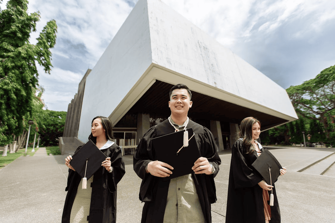 Graduates celebrating graduation outdoors in caps and gowns at a contemporary university campus.